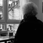 Seniorin sitzt gedankenverloren am Fenster