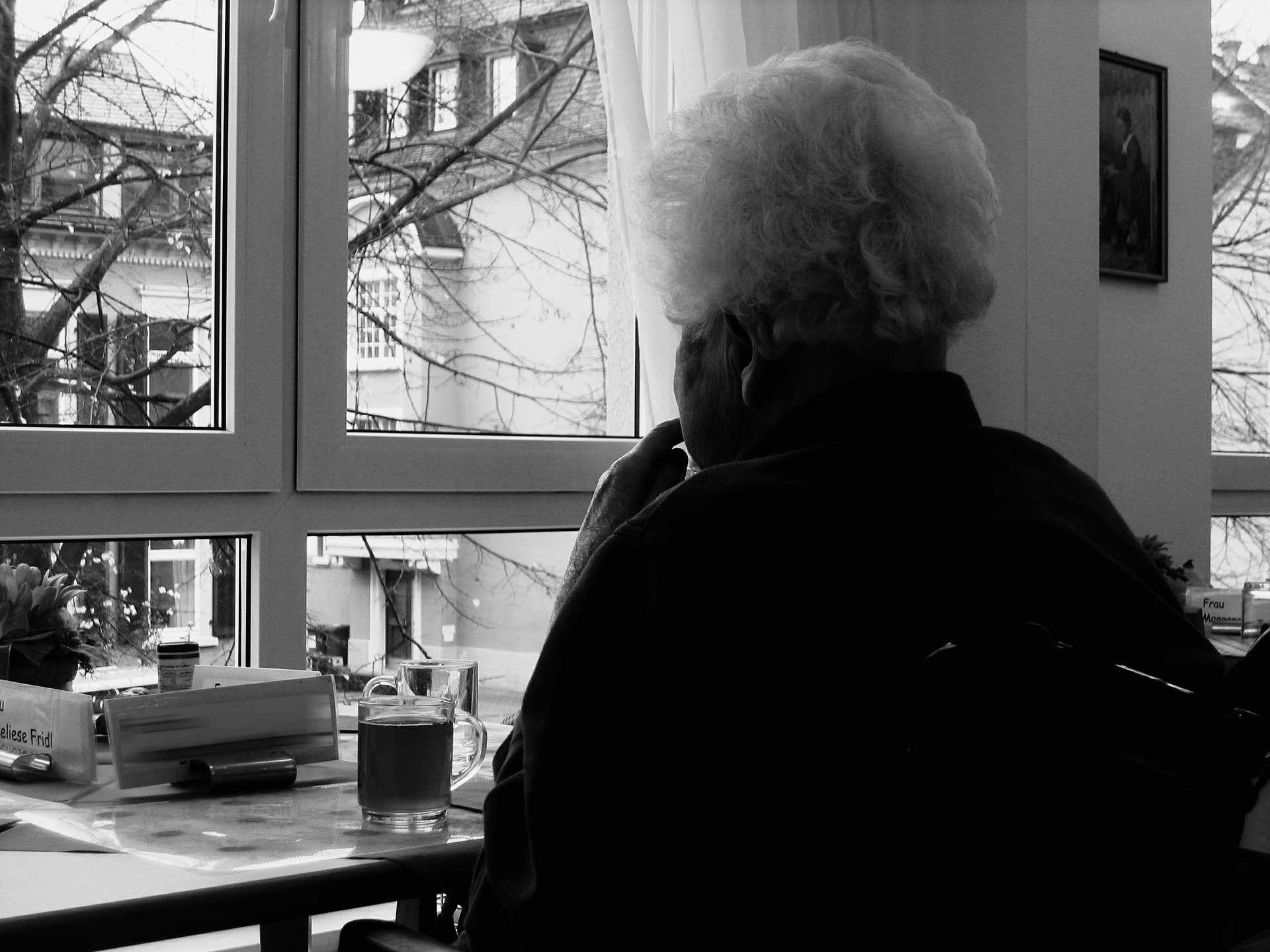 Seniorin sitzt gedankenverloren am Fenster